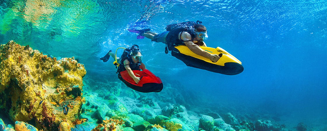 Two people riding seabob underwater scooters next to reef
